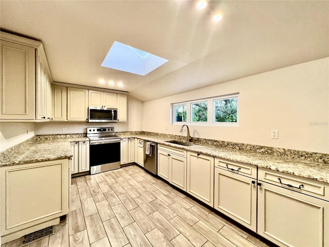 kitchen featuring sink, lofted ceiling with skylight, appliances with stainless steel finishes, light hardwood / wood-style flooring, and cream cabinetry