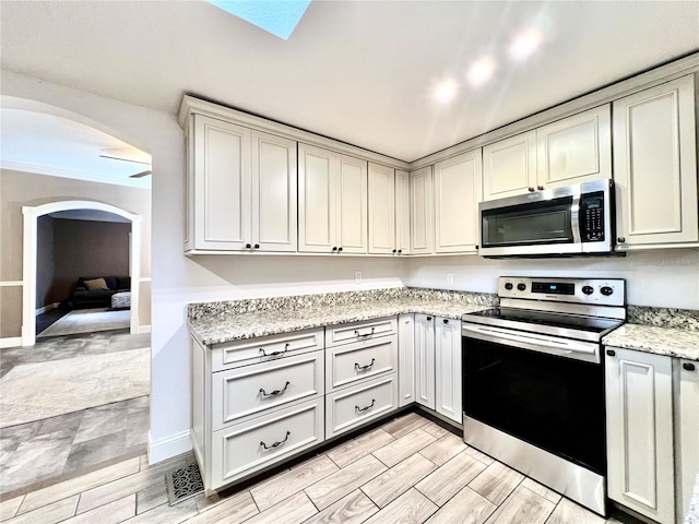 kitchen with a skylight, appliances with stainless steel finishes, light stone counters, and crown molding