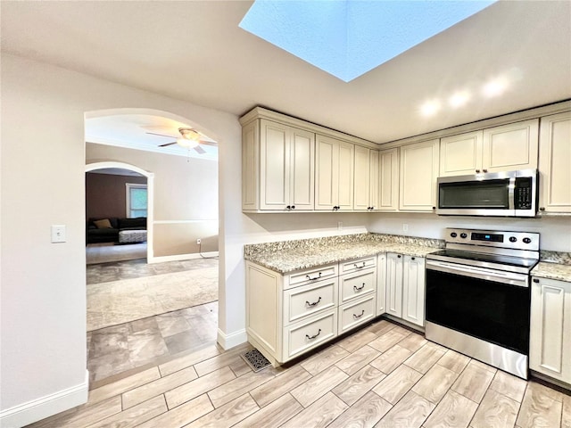 kitchen with stainless steel appliances, ceiling fan, light stone counters, and cream cabinetry