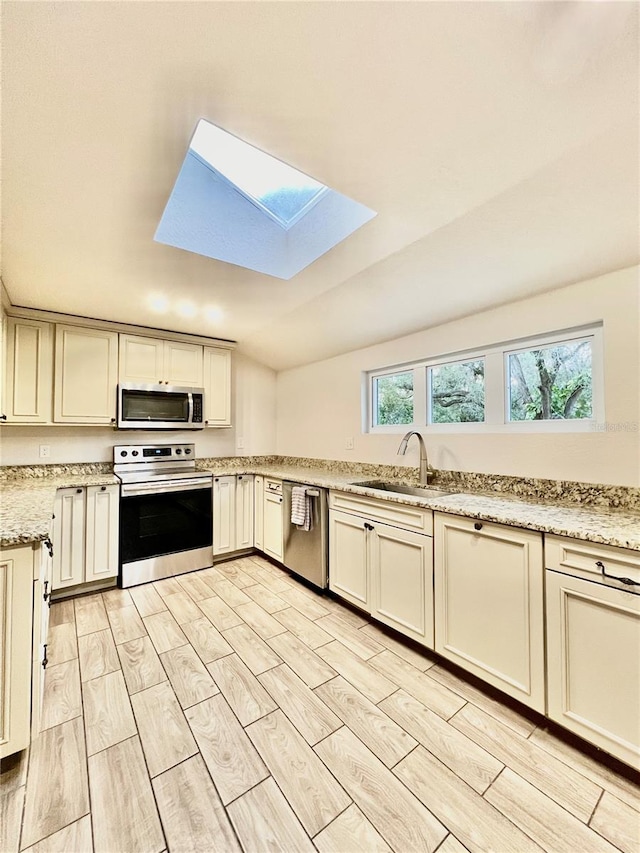 kitchen featuring sink, lofted ceiling with skylight, light stone countertops, light wood-type flooring, and appliances with stainless steel finishes