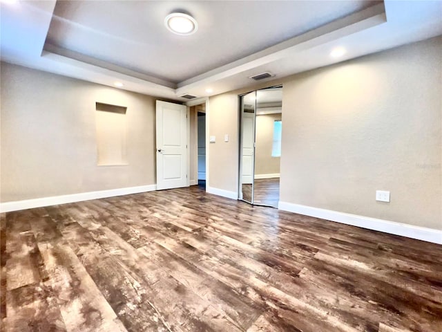 unfurnished bedroom featuring hardwood / wood-style flooring, a closet, and a tray ceiling