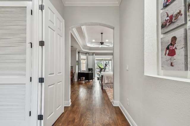 corridor with crown molding, dark wood-type flooring, and a tray ceiling