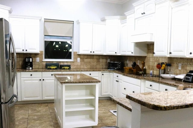 kitchen featuring stainless steel fridge, white cabinetry, a center island, tasteful backsplash, and dark stone counters