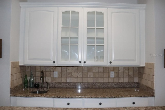 kitchen with tasteful backsplash, sink, white cabinets, and dark stone counters