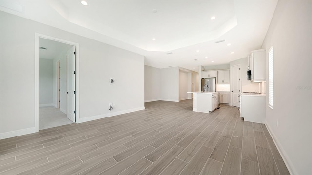 unfurnished living room with light hardwood / wood-style flooring and a tray ceiling