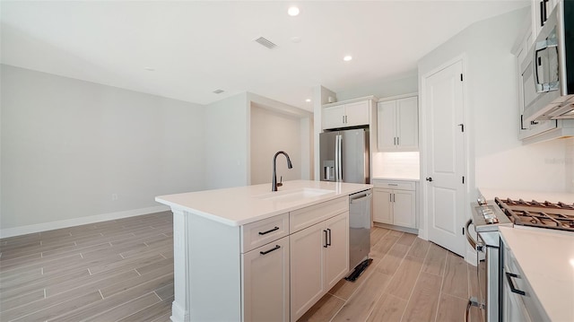 kitchen with light hardwood / wood-style flooring, a kitchen island with sink, stainless steel appliances, sink, and white cabinetry