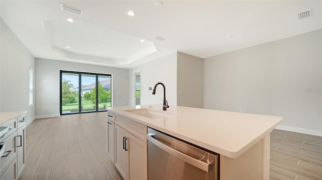 kitchen with light hardwood / wood-style flooring, dishwasher, an island with sink, sink, and a raised ceiling