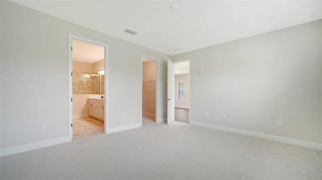 unfurnished bedroom with a closet, connected bathroom, light carpet, and a spacious closet