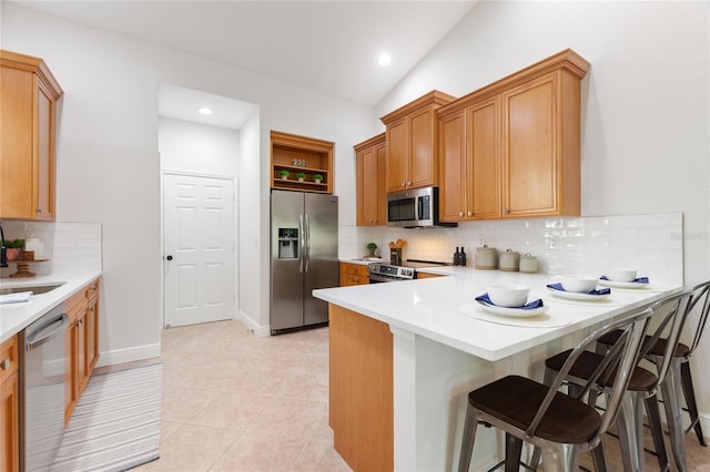 kitchen featuring appliances with stainless steel finishes, tasteful backsplash, lofted ceiling, light tile patterned floors, and a kitchen breakfast bar