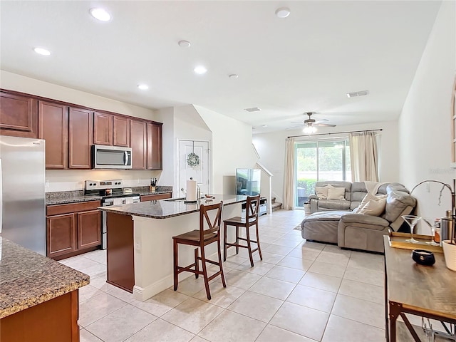 kitchen featuring light tile patterned floors, appliances with stainless steel finishes, an island with sink, and ceiling fan