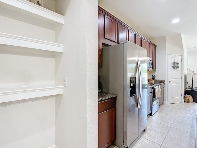 kitchen with light tile patterned flooring, appliances with stainless steel finishes, and dark stone countertops