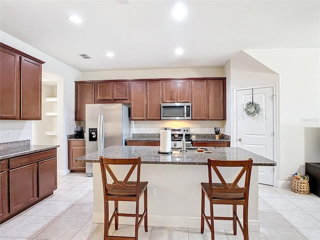 kitchen featuring appliances with stainless steel finishes, a kitchen island with sink, a breakfast bar area, and light tile patterned flooring