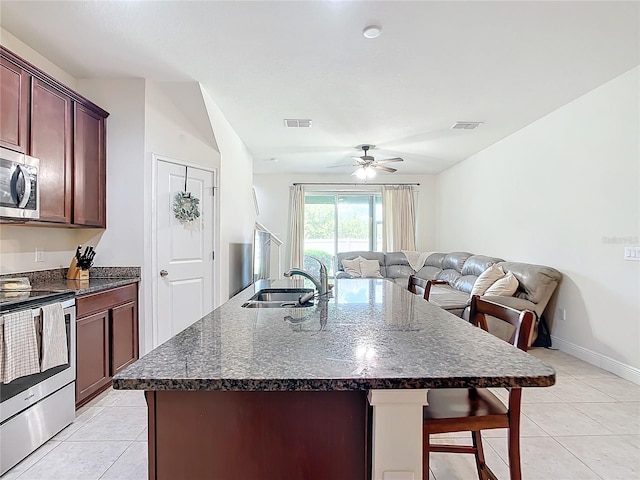 kitchen featuring stainless steel appliances, sink, light tile patterned flooring, ceiling fan, and a center island with sink