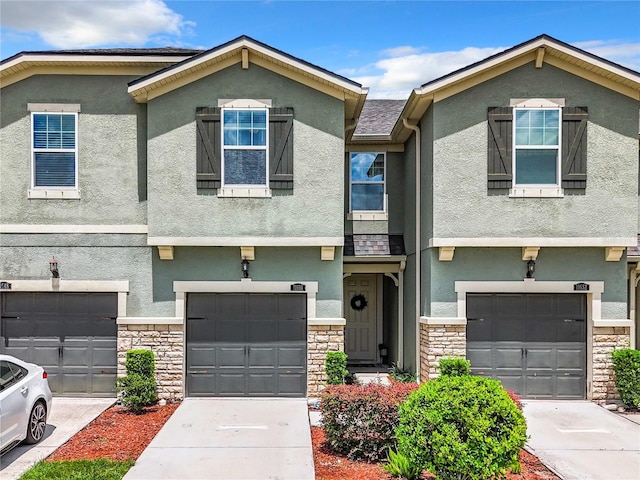 townhome / multi-family property featuring stone siding, driveway, and stucco siding