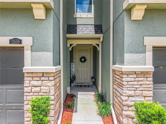 entrance to property featuring a shingled roof, stone siding, and stucco siding