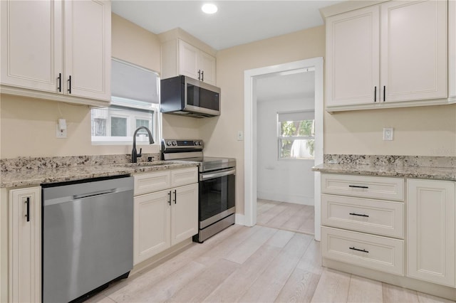 kitchen with light stone counters, light wood-type flooring, sink, and appliances with stainless steel finishes