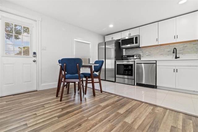 kitchen with light wood-type flooring, appliances with stainless steel finishes, white cabinetry, and tasteful backsplash