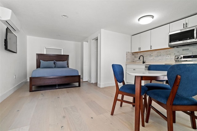 kitchen with a wall unit AC, light hardwood / wood-style floors, white cabinetry, stove, and decorative backsplash