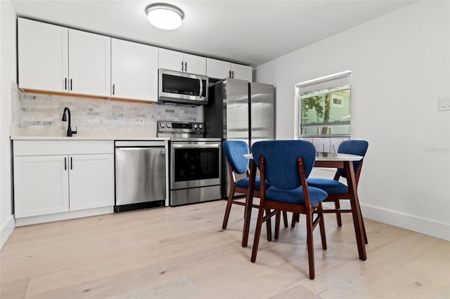 kitchen with white cabinets, backsplash, stainless steel appliances, and light hardwood / wood-style floors