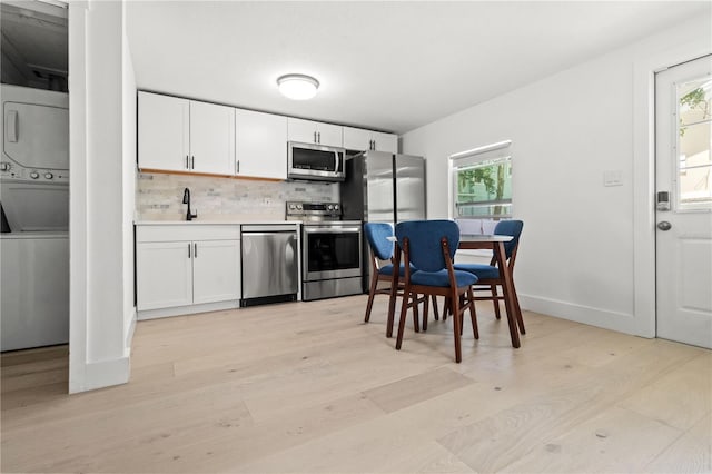 kitchen featuring stacked washer / drying machine, light wood-type flooring, appliances with stainless steel finishes, and white cabinetry