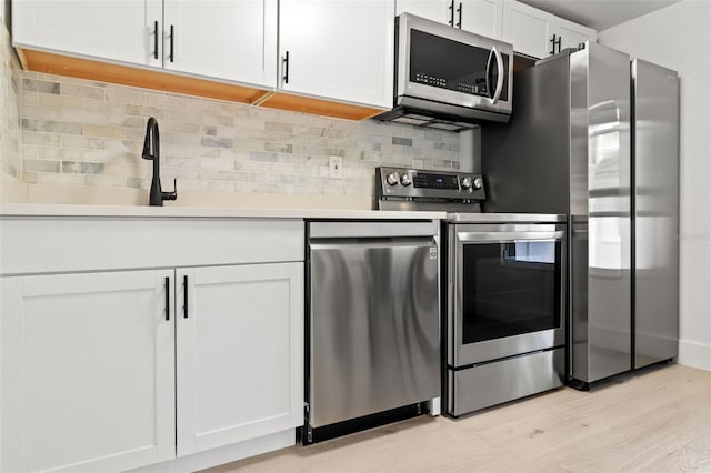 kitchen featuring white cabinets, decorative backsplash, stainless steel appliances, and light hardwood / wood-style floors