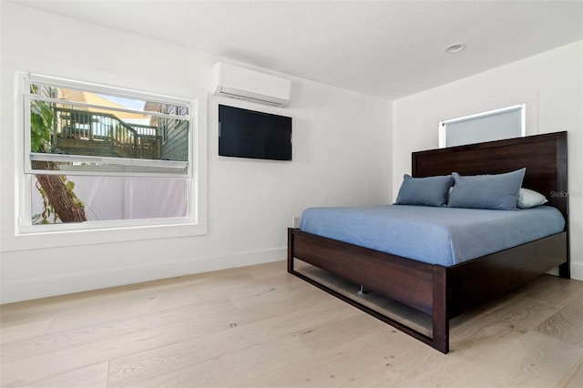 bedroom with a wall mounted AC and light hardwood / wood-style floors