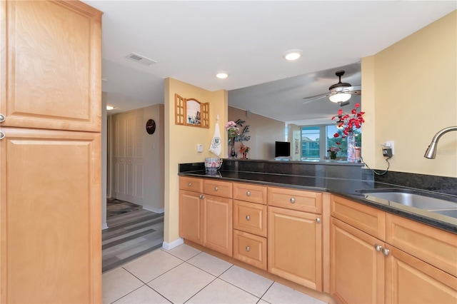 kitchen featuring dark stone counters, light brown cabinetry, sink, and light tile patterned floors