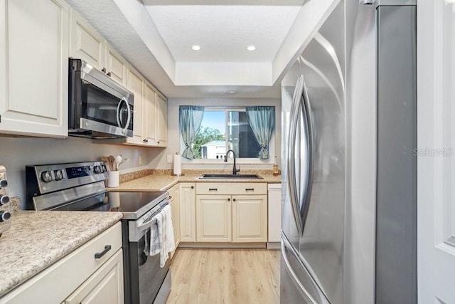 kitchen with light hardwood / wood-style floors, stainless steel appliances, sink, and a raised ceiling