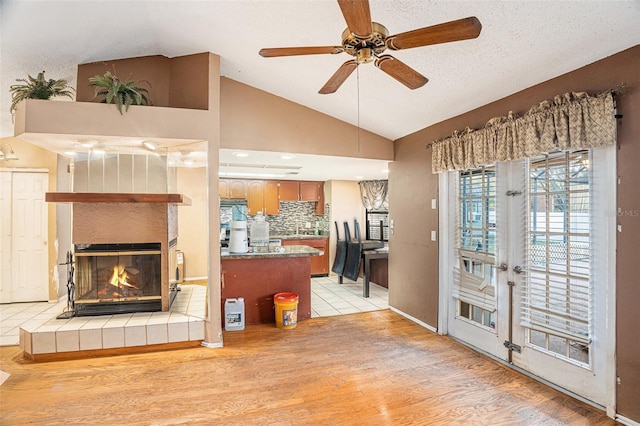 living room with light hardwood / wood-style flooring, vaulted ceiling, a textured ceiling, a fireplace, and ceiling fan