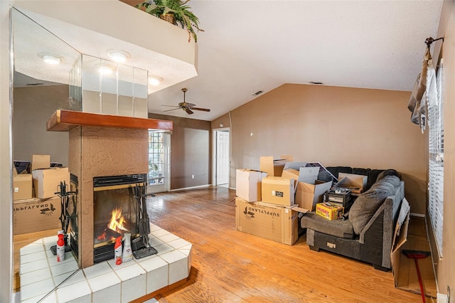 living room featuring a tiled fireplace, light hardwood / wood-style floors, vaulted ceiling, and ceiling fan