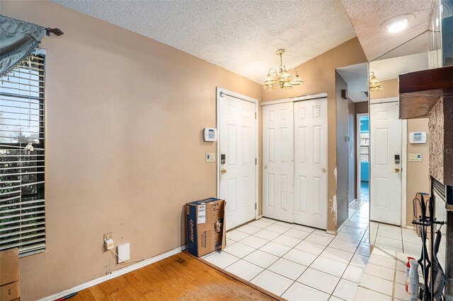 foyer entrance featuring light hardwood / wood-style floors, a textured ceiling, vaulted ceiling, and a chandelier