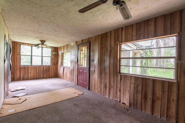 carpeted empty room with a textured ceiling, plenty of natural light, wood walls, and ceiling fan