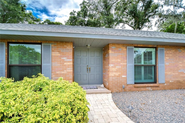 doorway to property featuring brick siding and roof with shingles