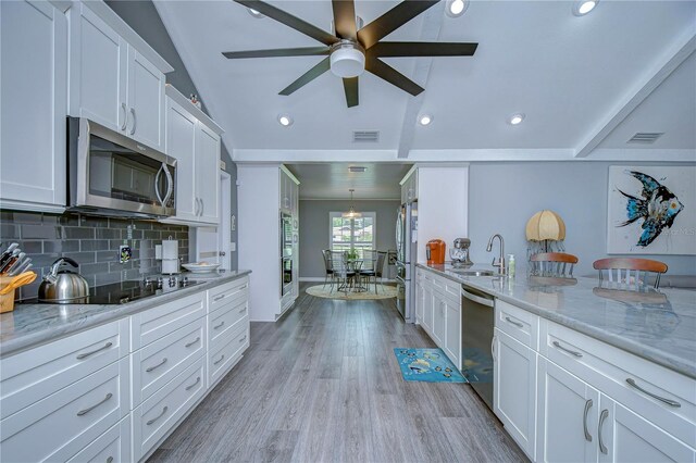 kitchen with white cabinets, vaulted ceiling, appliances with stainless steel finishes, sink, and ceiling fan