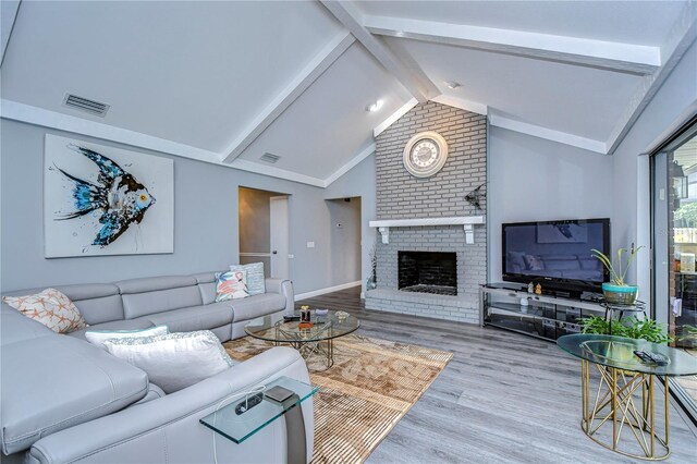 living room featuring light wood-type flooring, a fireplace, and lofted ceiling with beams