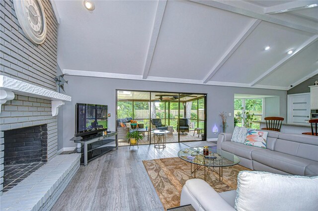 living room with hardwood / wood-style flooring, plenty of natural light, beamed ceiling, and a brick fireplace