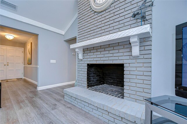 unfurnished living room with light wood-type flooring, a brick fireplace, and vaulted ceiling