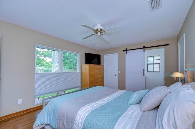 bedroom with a barn door, ceiling fan, and hardwood / wood-style flooring