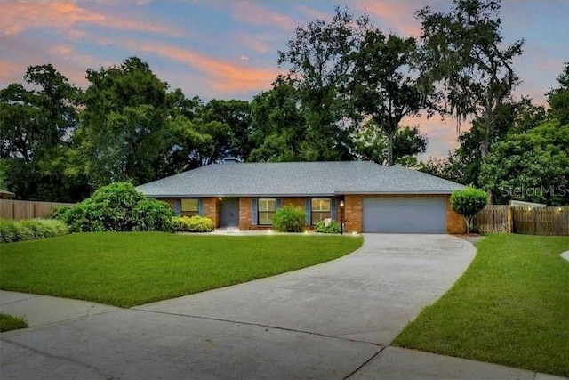 single story home featuring driveway, a garage, fence, a front yard, and brick siding