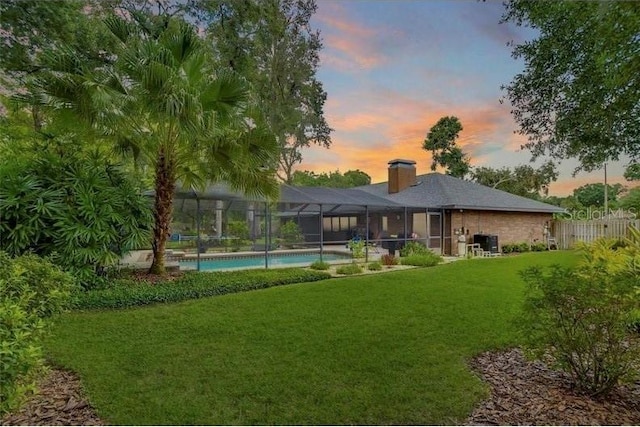 back house at dusk with a lawn and glass enclosure