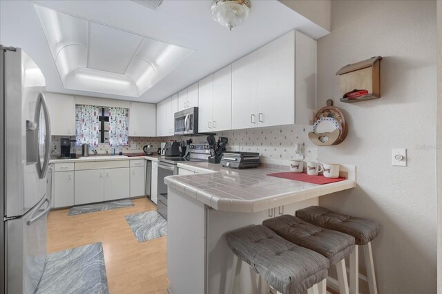 kitchen featuring stainless steel appliances, backsplash, tile counters, and white cabinets