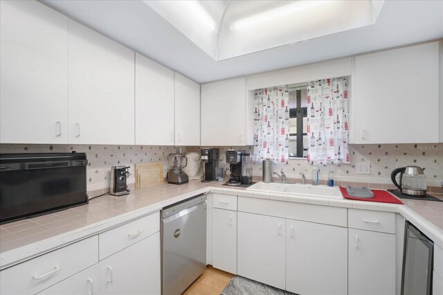 kitchen featuring decorative backsplash, white cabinetry, tile counters, stainless steel dishwasher, and sink