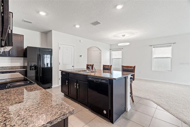 kitchen featuring a textured ceiling, black appliances, a kitchen island with sink, light carpet, and sink