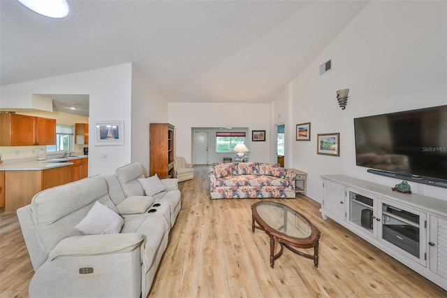 living room featuring sink, high vaulted ceiling, light hardwood / wood-style floors, and a healthy amount of sunlight