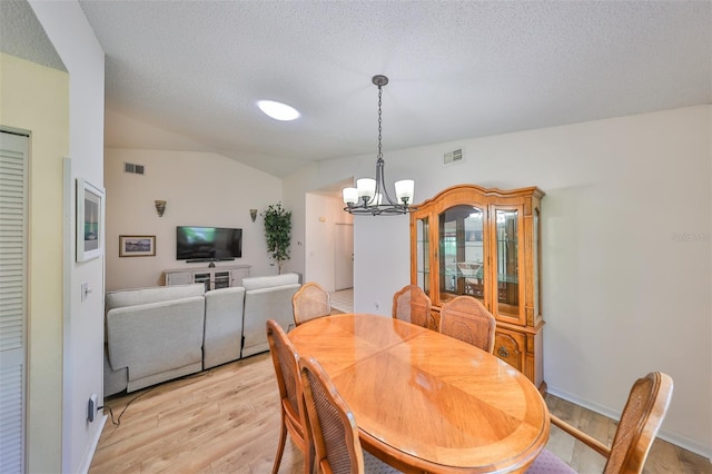 dining space featuring a textured ceiling, vaulted ceiling, an inviting chandelier, and light hardwood / wood-style floors