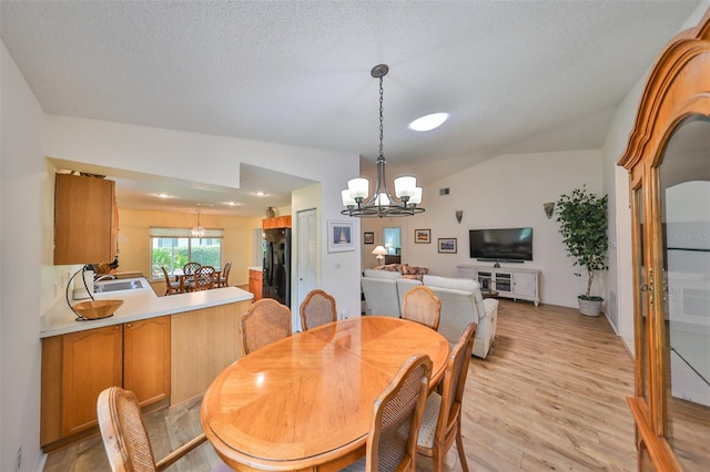 dining room featuring light hardwood / wood-style flooring, a chandelier, vaulted ceiling, sink, and a textured ceiling