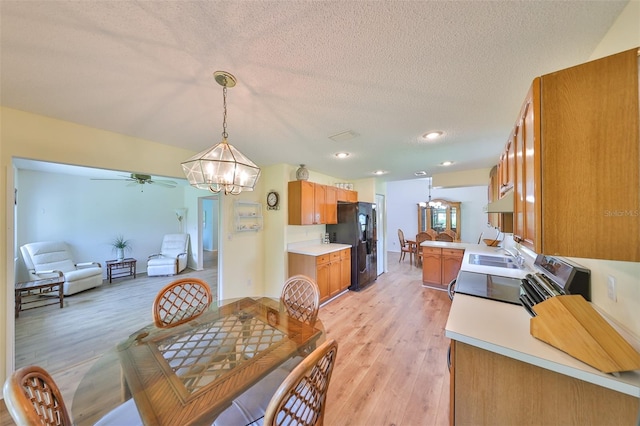 dining space featuring light wood-type flooring, ceiling fan with notable chandelier, sink, and a textured ceiling