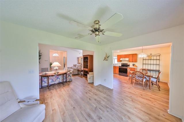 living room featuring ceiling fan, light wood-type flooring, and a textured ceiling