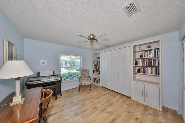 living area with ceiling fan, light hardwood / wood-style flooring, and a textured ceiling