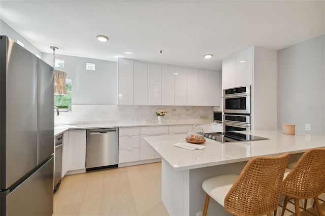 kitchen featuring white cabinetry, a breakfast bar, stainless steel appliances, and light hardwood / wood-style flooring